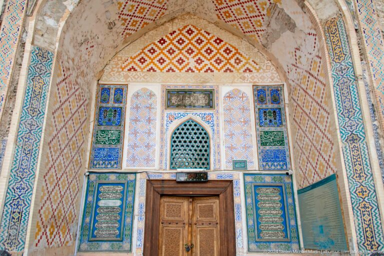 Pointed arched bay with carved wooden doors and blue-green tile decoration.