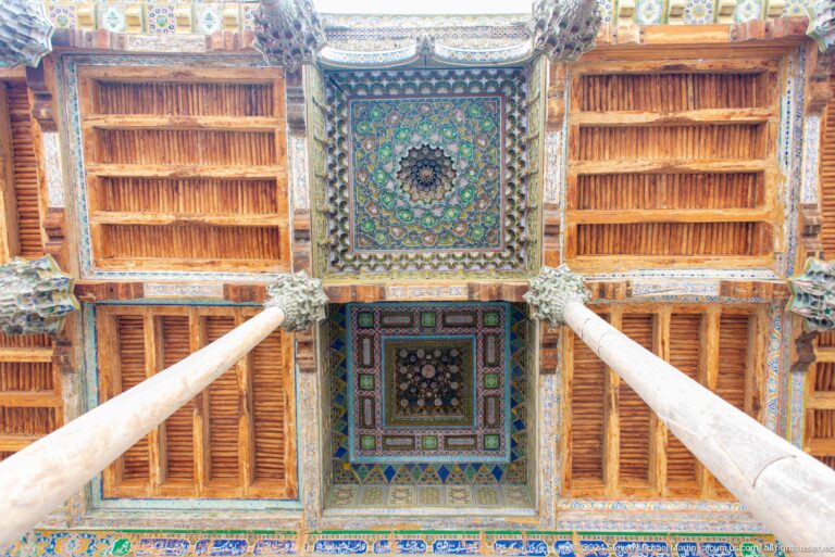 Upward view through wooden columns to a painted geometric ceiling.
