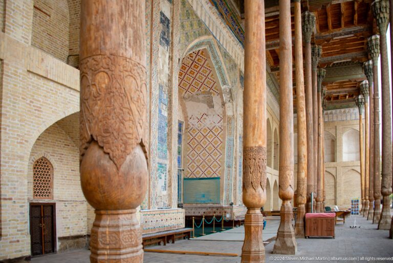 Long row of carved wooden columns beside a tiled mosque façade.
