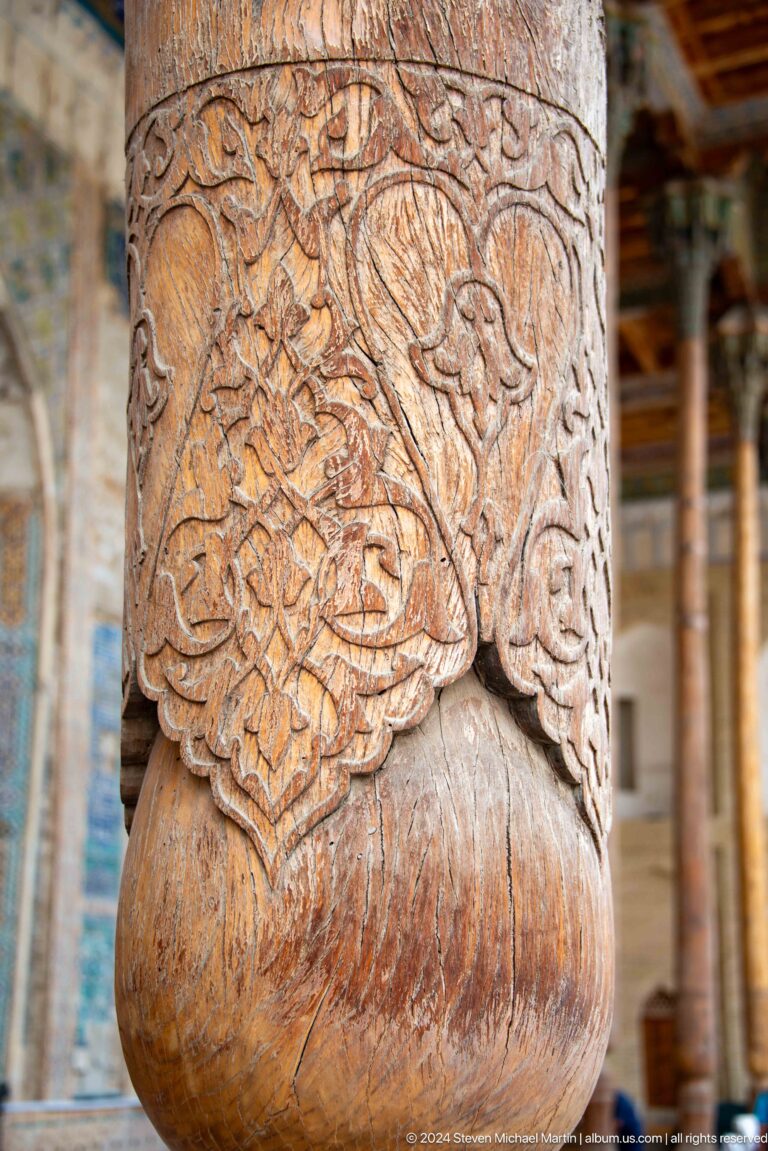 Close-up of floral carving on a weathered wooden mosque column.