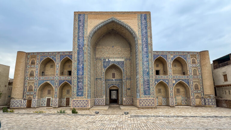Frontal façade of a tiled madrasa with a tall central entrance iwan.