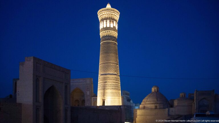Illuminated Kalyan Minaret rising above low domes at blue hour.
