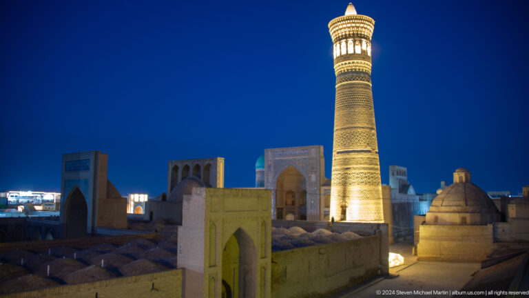 Elevated night view of Kalyan Minaret above domes and historic buildings.