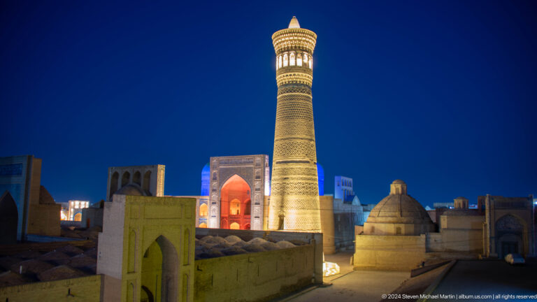 Kalyan Minaret above domed roofs and a red-lit portal at night.