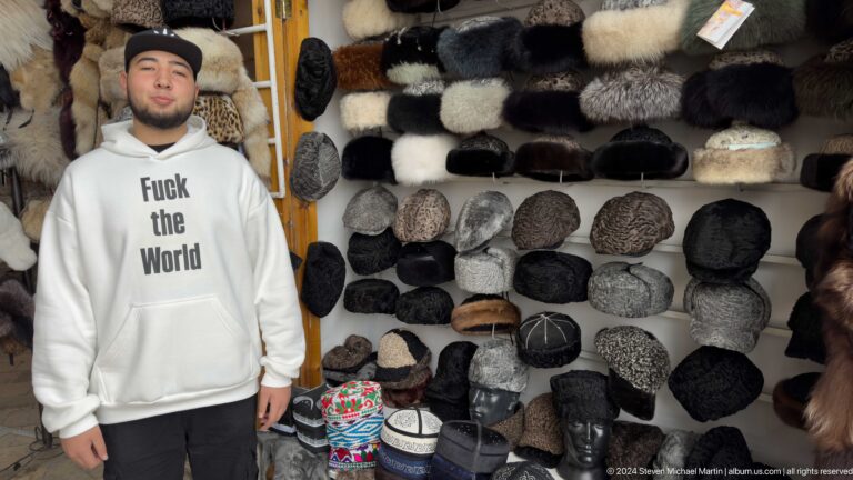 Wall display of dark and light fur hats with a visitor at left.