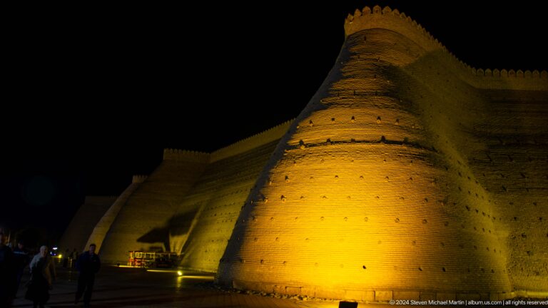 Illuminated curved defensive wall of the Ark of Bukhara at night.