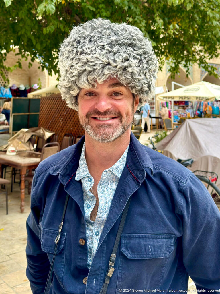 Smiling gray-haired man seated at an outdoor market in Bukhara.