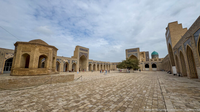 Wide stone-paved Kalyan Mosque courtyard enclosed by pointed arcades.