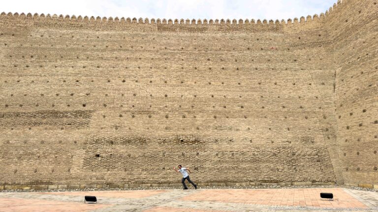 Long crenellated wall of the Ark of Bukhara with a pedestrian below.