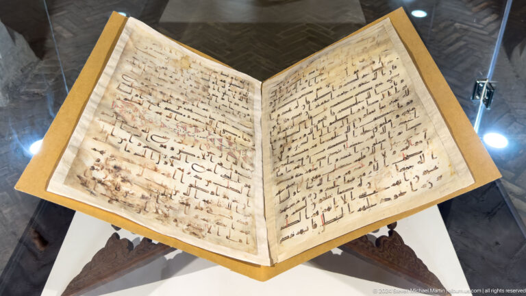 Open Arabic manuscript displayed on a carved wooden book stand.