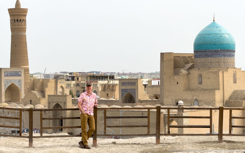 Man in a pink shirt overlooking a turquoise dome and historic Bukhara.