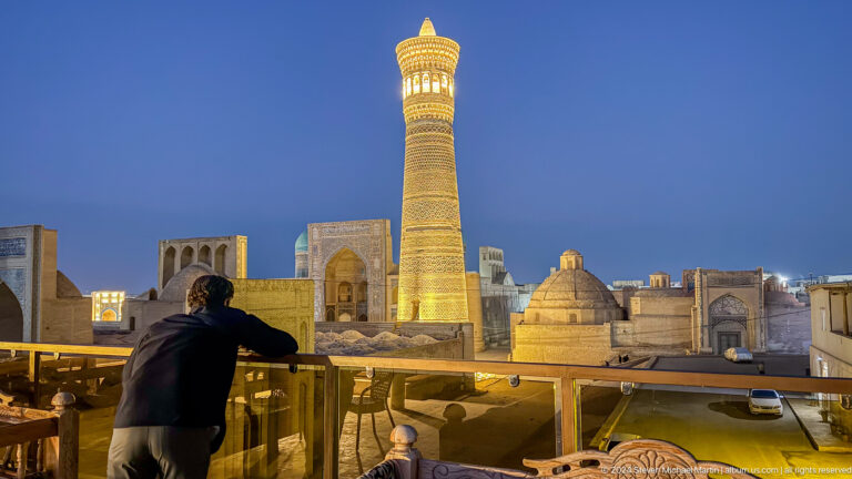 Visitor at a rooftop railing facing the illuminated Kalyan Minaret.