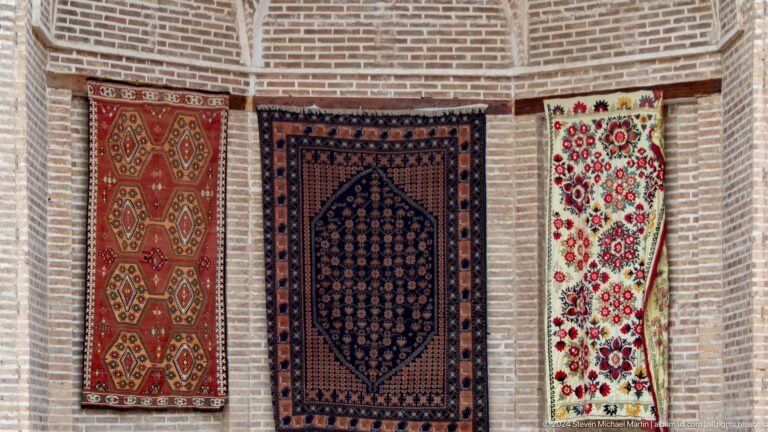 Three patterned carpets hanging on brick wall.