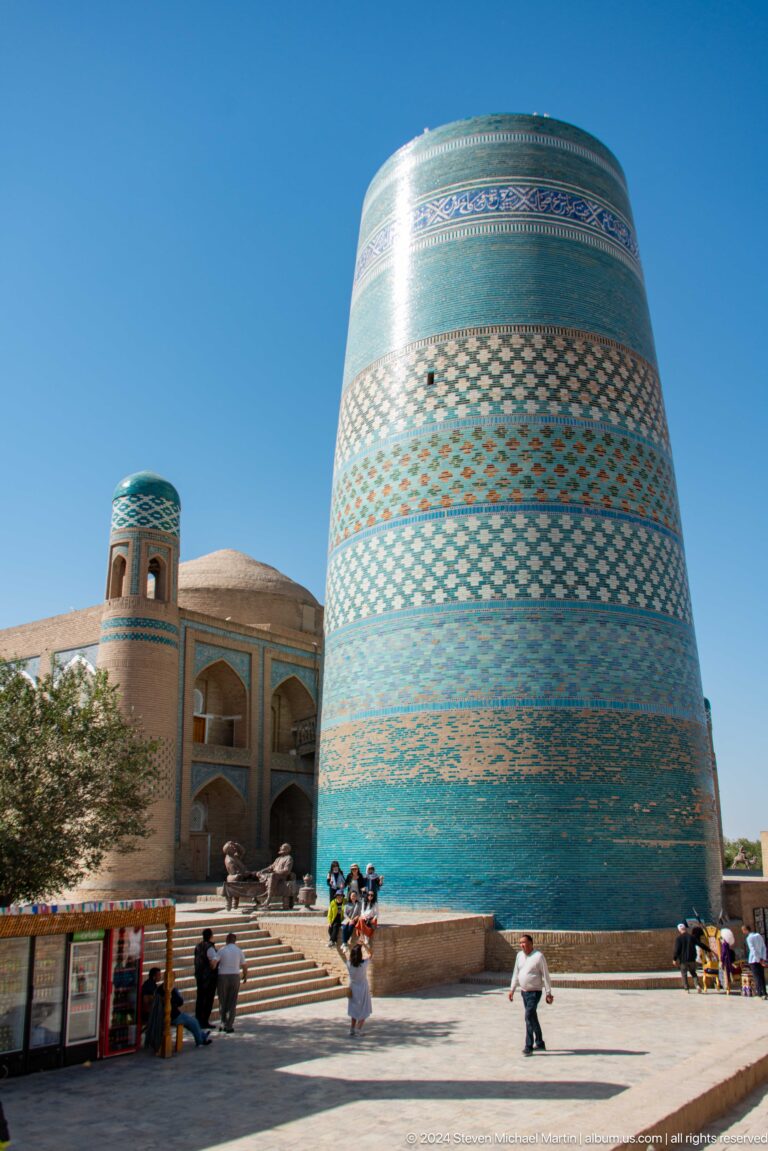 Kalta minor rising beside a smaller tiled minaret and dome.