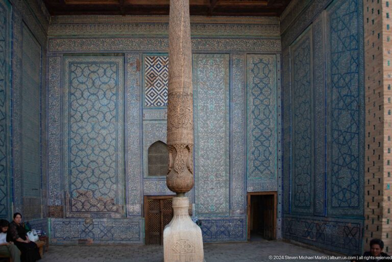 Carved wooden column before blue tiled wall.