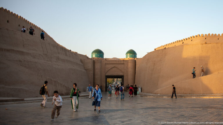Visitors crossing broad courtyard before fortified gate.