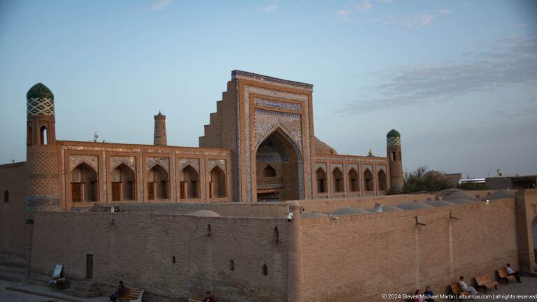 Madrasa facade seen over defensive wall at dusk.