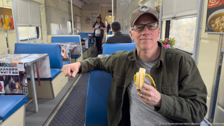 Smiling traveler holding a banana in train dining car.