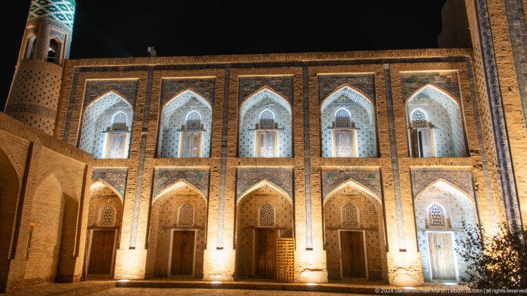 Floodlit two-story madrasa facade at night.