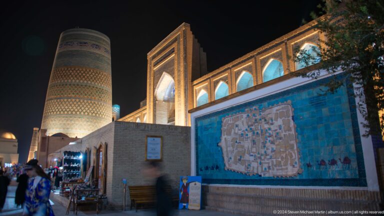 Night street with illuminated wall map and madrasa facade.