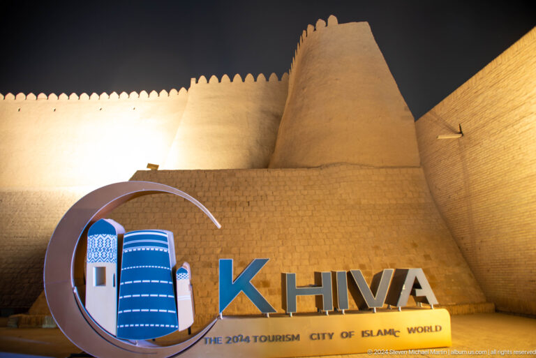 Illuminated khiva city sign before crenellated wall.