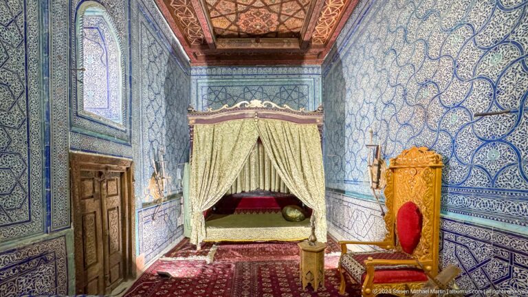 Wider palace bedroom view with throne-like chair.