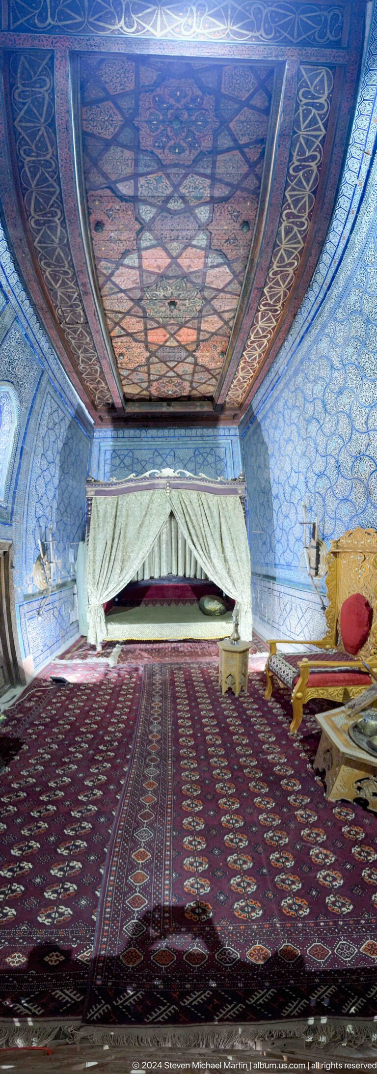 Closer view of canopied bed and blue patterned walls.