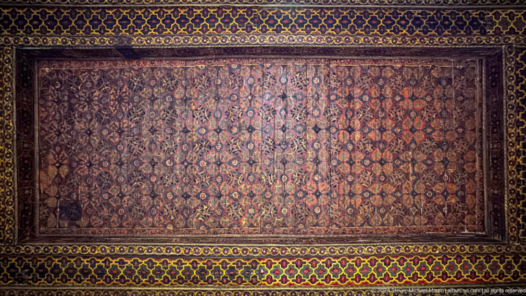 Large patterned carpet displayed on wall.