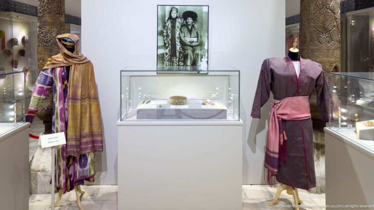 Museum mannequins in historic garments beside display case.