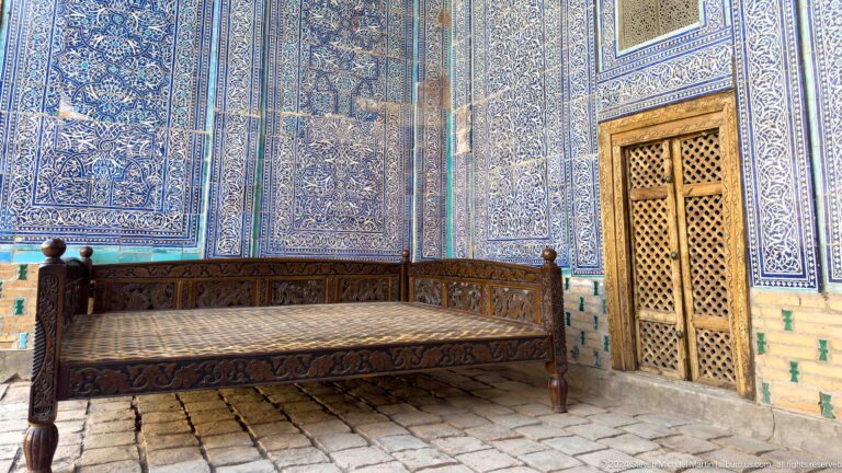 Wooden bench and carved door against blue-tiled wall.