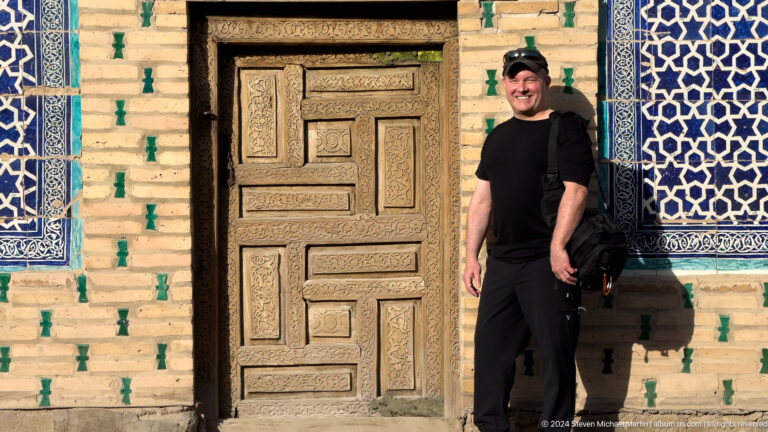 Man in black standing beside carved historic door.