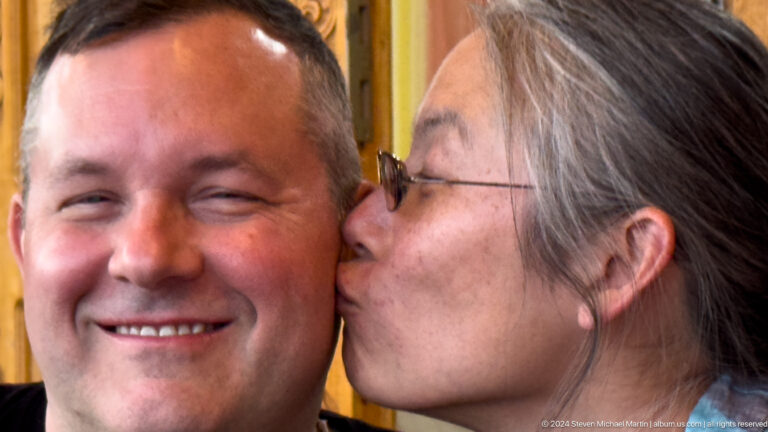Woman kissing smiling man on cheek.