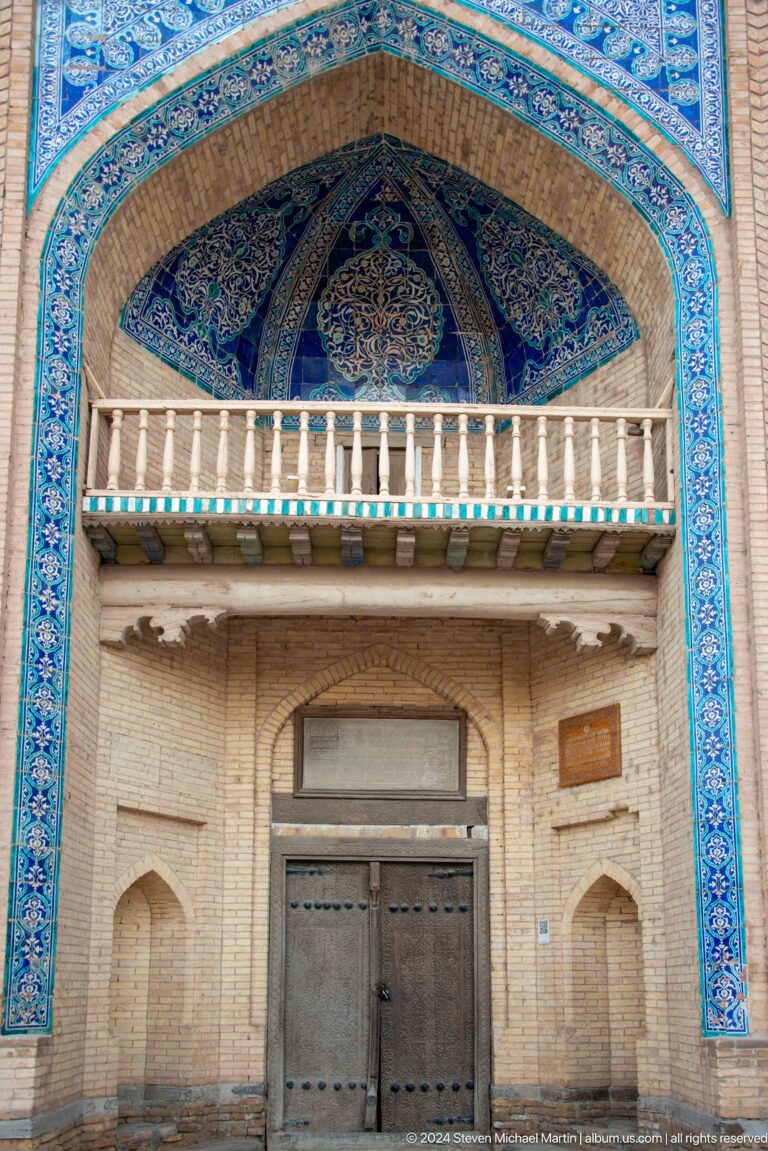 Carved wooden balcony above tiled and brick facade.