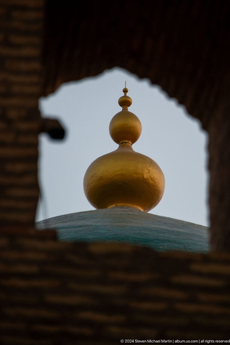 Gold finial atop green dome seen through arch.
