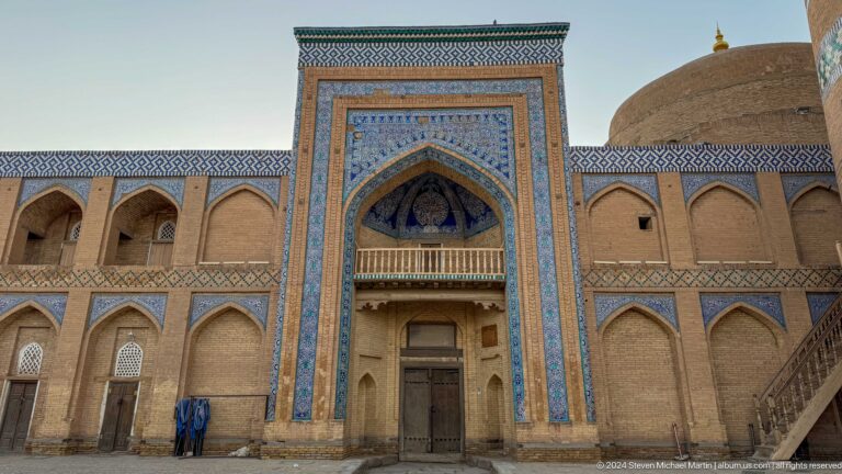 Ornate madrasa facade with tiled portal and dome.