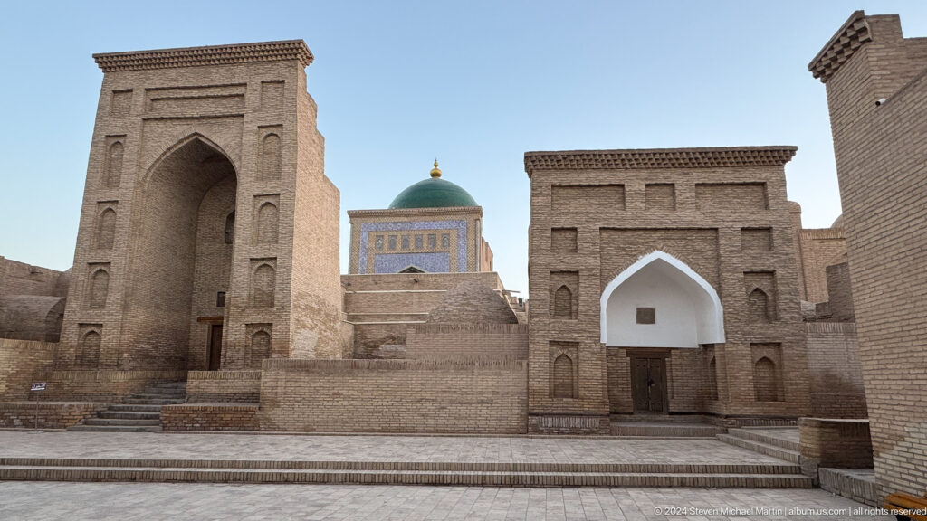 Green dome framed by brick mausoleum and madrasa walls.