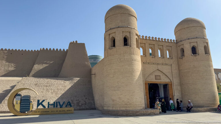 Whitewashed ata darvaza gate with visitors entering.