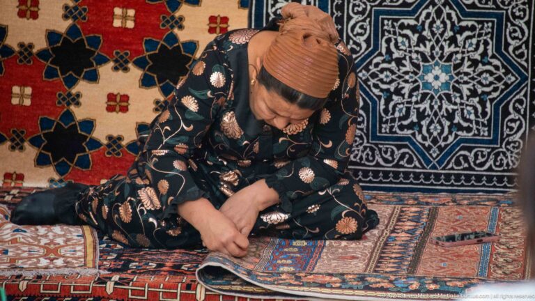 Craftswoman embroidering a textile at a market stall.