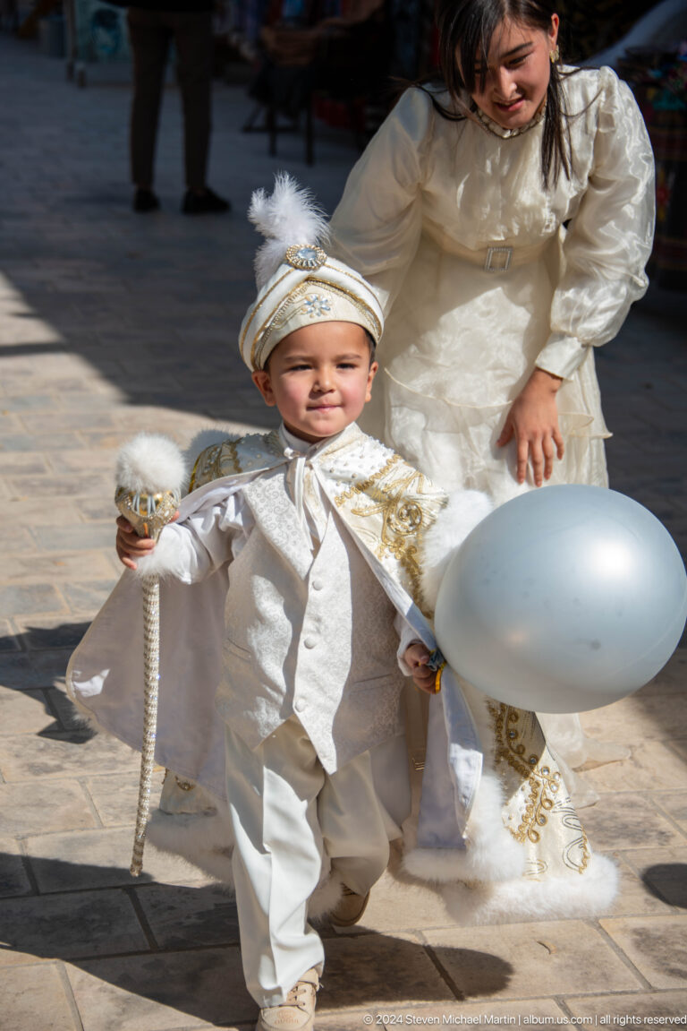 Young boy in ceremonial white clothing holding balloon and ornament.