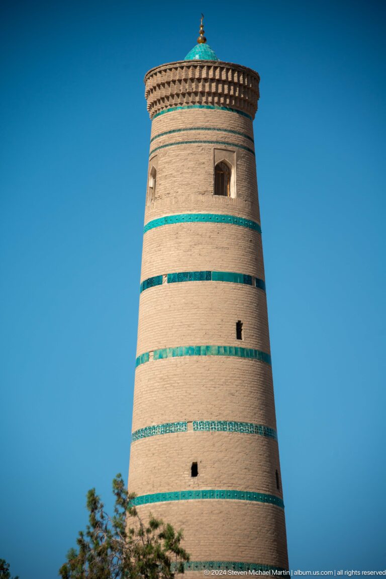 Plain tapering brick minaret with turquoise bands.