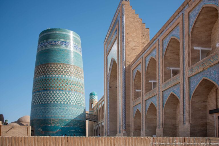 Kalta minor beside a long arcaded madrasa facade.