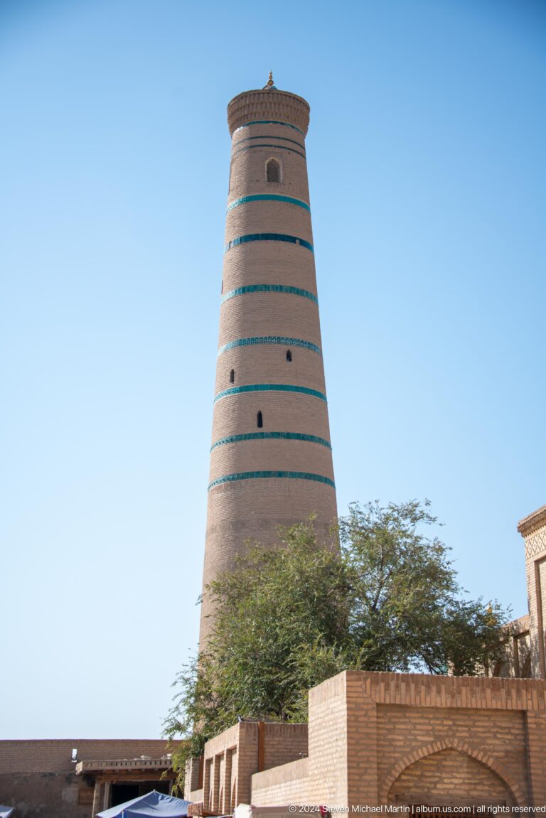 Tall tapering brick minaret with turquoise bands.