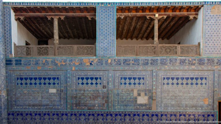 Long blue-tiled wall beneath carved wooden balcony.