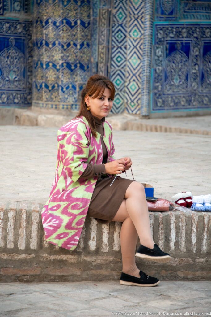 Woman in patterned coat seated by craft display.