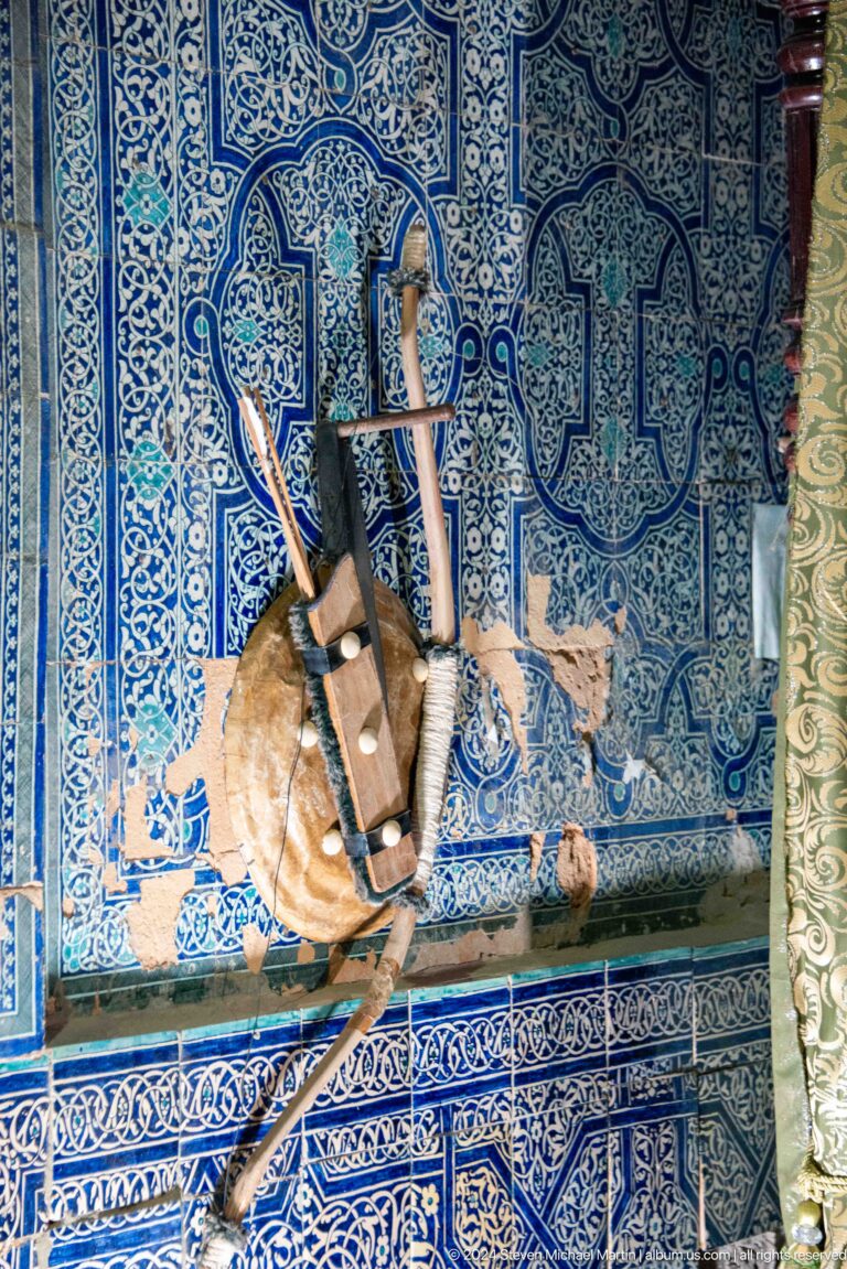 Historic firearms and leather gear mounted on tiled wall.