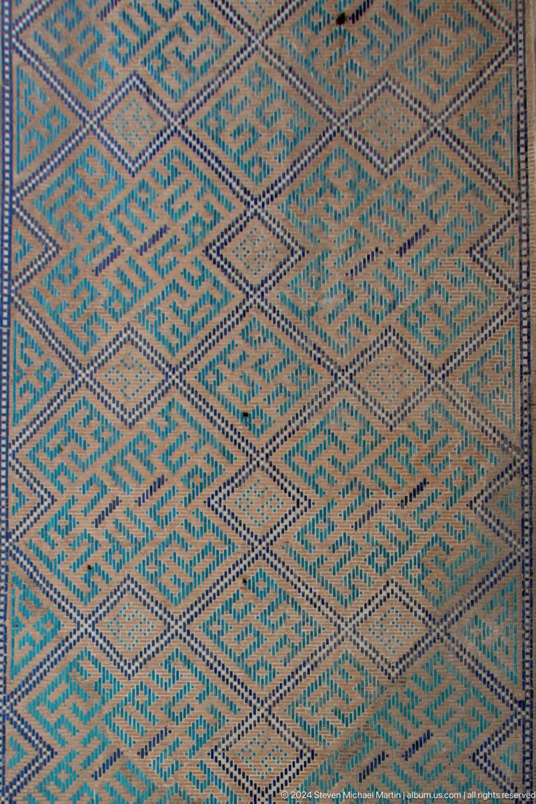 Close-up of turquoise, cream, and dark-blue geometric tile mosaic with interlocking angular motifs.