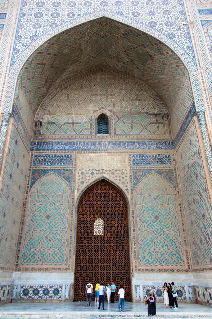 Tall tiled portal recess with a pointed wooden-lattice doorway, geometric side panels, and a small upper window.