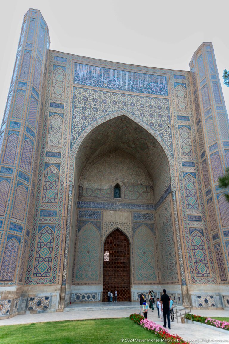 Low-angle view of a towering pointed iwan with turquoise tile borders and a small doorway at its base.
