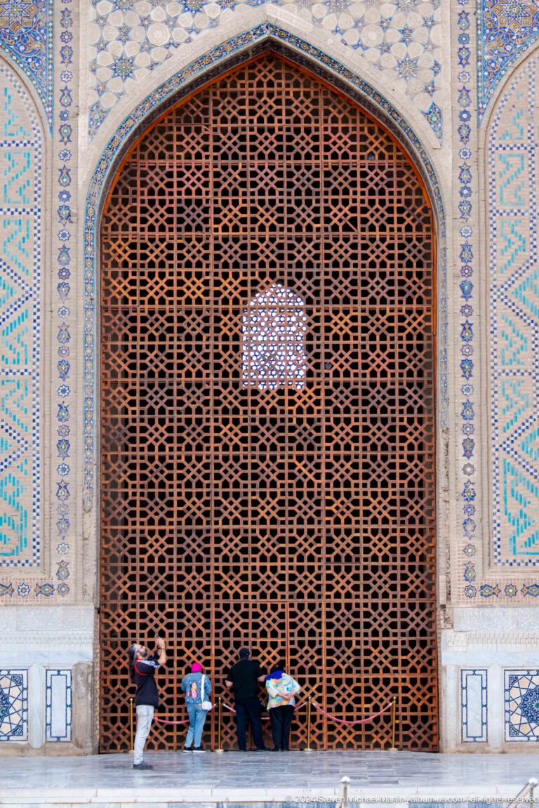 Reddish geometric wooden lattice with a small pointed opening, framed by pale blue and turquoise tiles.