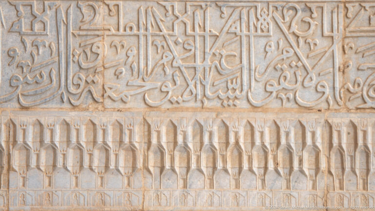 Close-up of a pale carved calligraphic frieze above a row of faceted geometric ornamental forms.